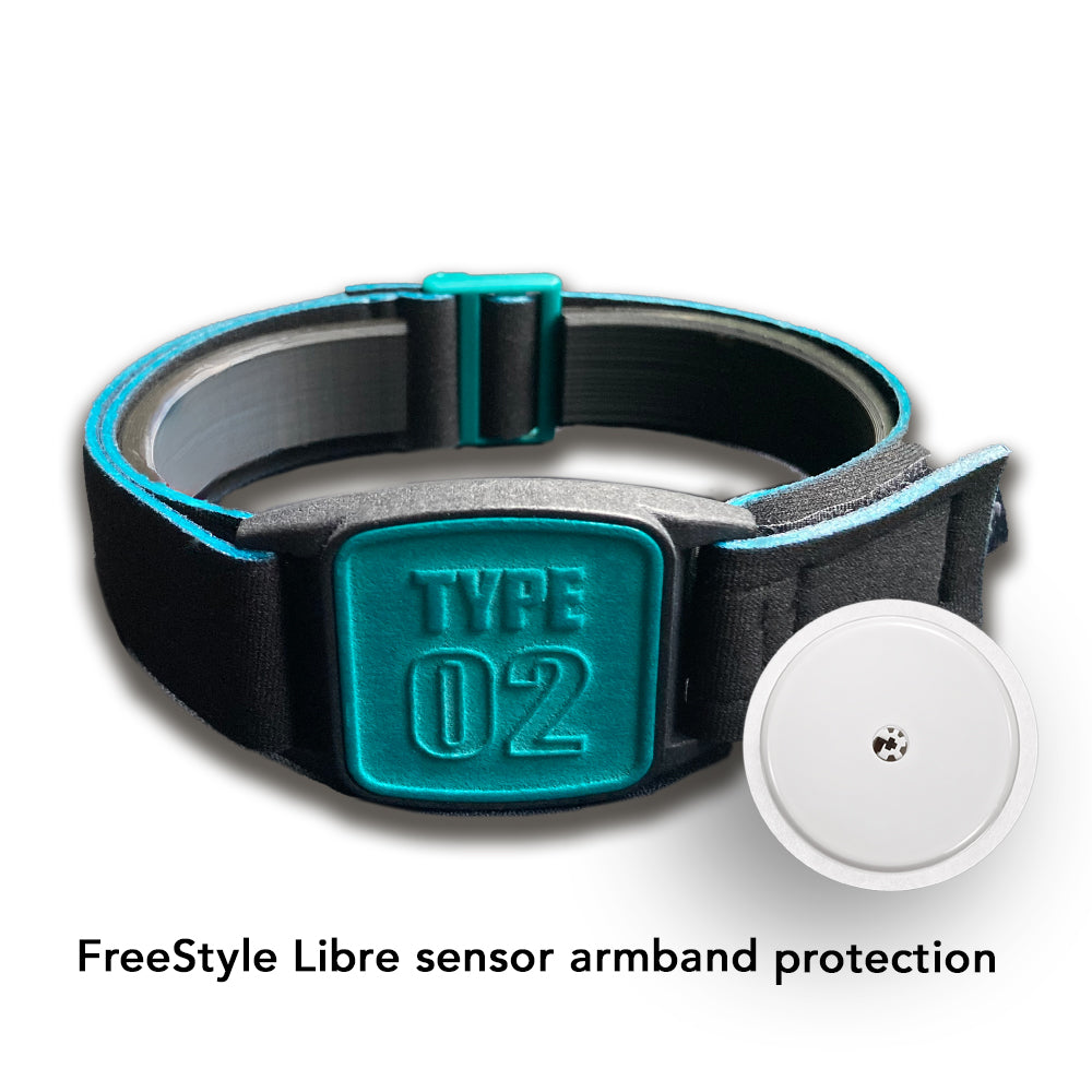 A Freestyle Libre 2 CGM sports and swim armband in teal and black, placed on a wooden surface near a white towel and a pool.