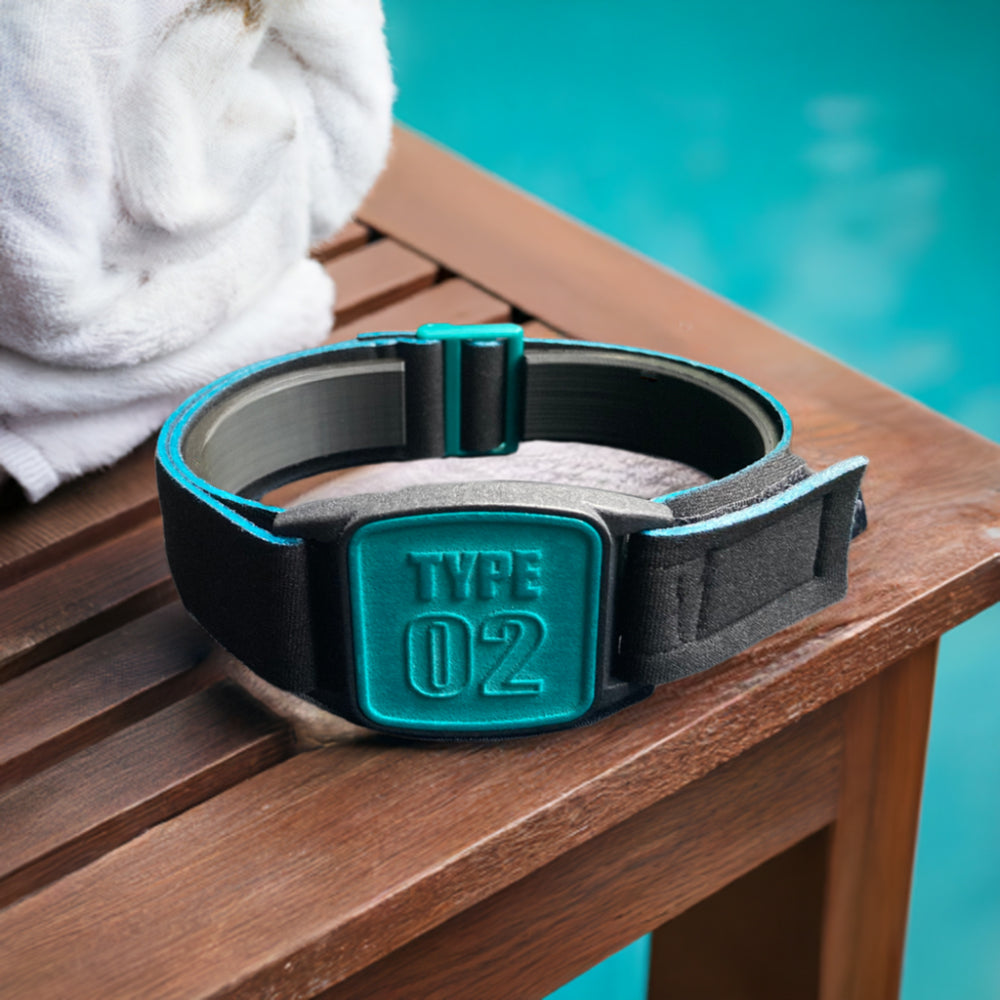 A Freestyle Libre 2 CGM sports and swim armband in teal and black, placed on a wooden surface near a white towel and a pool.