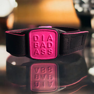 Libreband CGM armband for FreeStyle Libre 2 with magenta DIABADASS cover and black water-resistant neoprene strap on reflective glass surface. LML4108, LML4115, LML4122, LML4474.